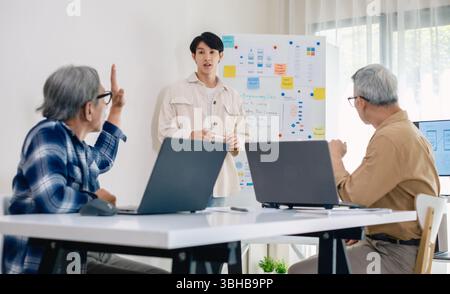 senior programmer bootcamlp,Asian young instructor guides senior learners through a programming on whiteboard, highlighting algorithm thinking and sim Stock Photo