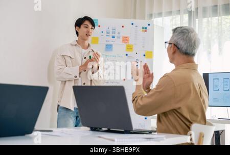 senior programmer bootcamlp,Asian young instructor guides senior learners through a programming on whiteboard, highlighting algorithm thinking and sim Stock Photo