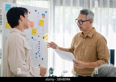 senior programmer bootcamlp,Asian young instructor guides senior learners through a programming on whiteboard, highlighting algorithm thinking and sim Stock Photo