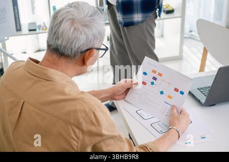 Senior programmer planning software development with flowchart and system process documentation at office Stock Photo
