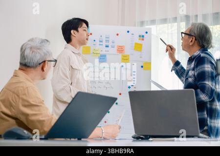 senior programmer bootcamlp,Asian young instructor guides senior learners through a programming on whiteboard, highlighting algorithm thinking and sim Stock Photo