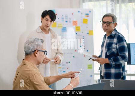 senior programmer bootcamlp,Asian young instructor guides senior learners through a programming on whiteboard, highlighting algorithm thinking and sim Stock Photo