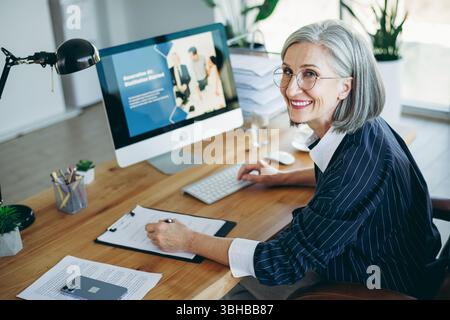 Elegant mature businesswoman working in a modern office space, showcasing professionalism and charm while completing tasks Stock Photo