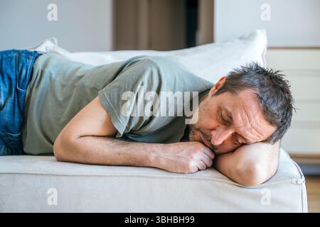 Desperate sad man laying on sofa couch, feeling miserable and depressed, selective focus Stock Photo