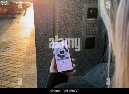 A Person's Hand Holding Smartphone For Disarming Security System Of Door Stock Photo