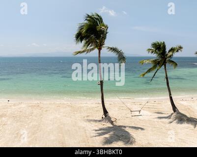Hammock strung between palm trees overlooking a tranquil turquoise sea and a pristine sandy beach. Haad Yuan Beach. Ko Pha Ngan, Thailand. Stock Photo