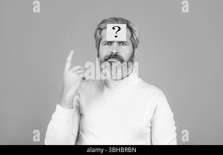 Thoughtful young man and sticky note with question mark on his forehead against. Beard man question mark in head, solution problems. Paper notes with Stock Photo