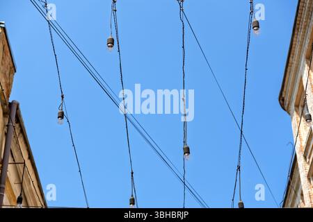 Decorative String Lights Garland with Retro Bulbs Hanging Between Old Buildings Against a Clear Sky.Urban Street Decoration: A Garland of Light Bulbs Stock Photo
