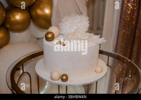 A pristine white, three-tiered cake adorned with delicate feathers and gold spheres sits elegantly on a metallic tiered stand, creating a luxurious de Stock Photo