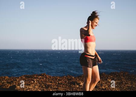 A female trail runner stands with ocean in background Stock Photo