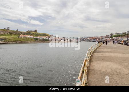 Looking down Whitby’s West Pier with the River Esk to the left, East Cliff’s historic buildings beyond, and the town stretching into the distance. Stock Photo