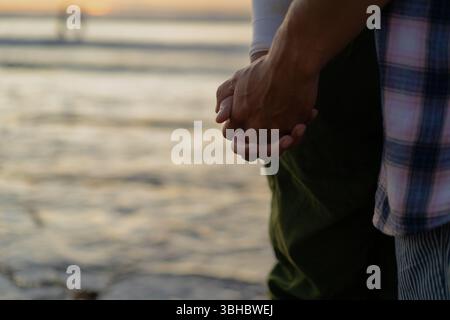 Close-up of couple holding hands at the beach during sunset Stock Photo
