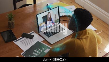 Image of spinning globe over african american woman having a image call on laptop at home. Global networking and business technology concept Stock Photo