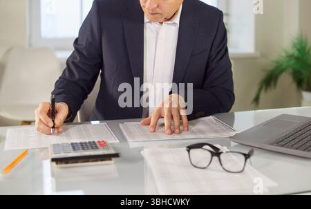Mature businessman working at desk with calculator, laptop in office, using online app, learning Stock Photo