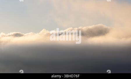 Layers of mist and clouds illuminated by the soft morning sunlight, creating a dreamy atmospheric scene perfect for creative backgrounds Stock Photo