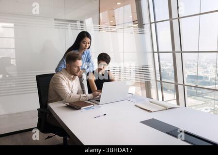 Three young multiracial colleagues working on joint task using laptop Stock Photo