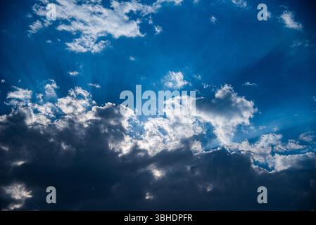 The photo shows a dramatic sky where bright sun rays break through thick clouds. The combination of light and shadow creates a striking and inspiring Stock Photo