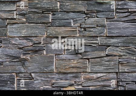 Close-up of a decorative wall with stacked slate stone cladding. Natural rock texture ideal as a background for architectural or interior design. Stock Photo