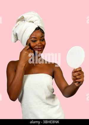 Young woman wearing towel using a gua sha scraping massage tool on her face after shower Stock Photo