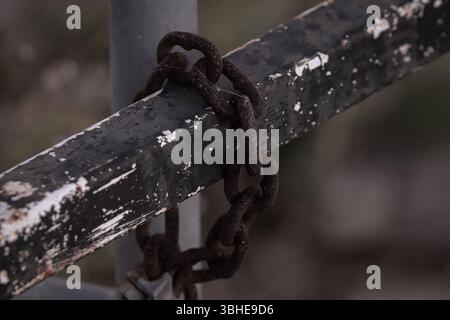 A rusty abandoned link of chains on a chipping iron fence. Stock Photo