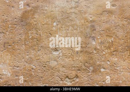 Detail of texture on weathered stone wall with historic graffiti inscriptions carved into the surface. Oxfordshire, UK. Stock Photo