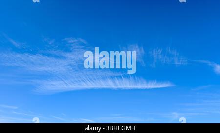 Delicate cirrus clouds drift across a clear blue sky with a faint airplane contrail visible in the distance. Stock Photo