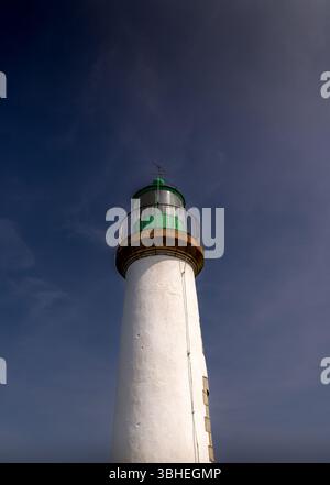 Upward view of a tall white lighthouse with a green lantern room, set against a deep blue sky on a sunny day. Stock Photo