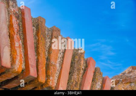 Textured bricks arranged in a stair-like formation rise against a bright blue sky. The sun casts soft shadows, emphasizing the intricate details and w Stock Photo