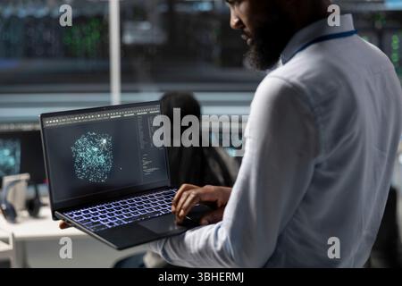 Data center engineer uses AI visualization tool on laptop to optimize resource allocation. Server hub IT expert uses artificial intelligence analysis on notebook to do maintenance Stock Photo