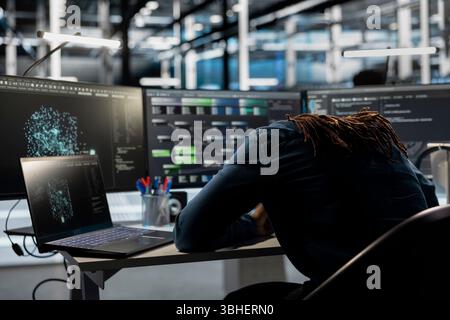 Exhausted server farm engineer falls asleep while looking at data analysis graph to reduce equipment failure. Tired data center worker exhausted after looking at AI visualization dashboard all day Stock Photo