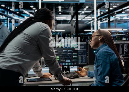Data center manager supervising work done by engineer using artificial intelligence neural networks. Supervisor overseeing worker in server room using AI programming language to configure hardware Stock Photo