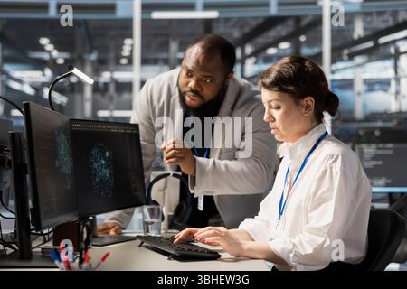 Data center manager supervising worker using artificial intelligence neural networks tech. Server farm team leader overseeing engineer using AI programming language on computer to update equipment Stock Photo