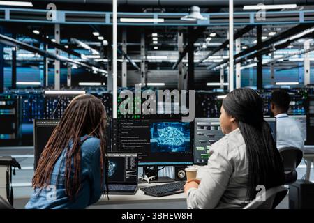 Data center engineering team working together, using AI visualization to oversee automated repetitive tasks. Server farm teamworking colleagues modifying systems based on data analytics graphs Stock Photo
