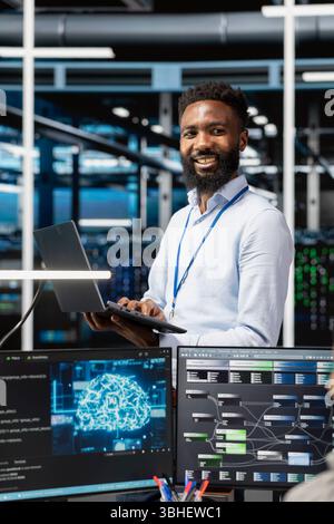 Cheerful man in server hub facility using artificial intelligence to perform demanding computing tasks. Jolly admin in data center uses AI technology for machine learning workloads Stock Photo