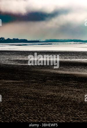 A vast expanse of tidal flats stretches out under a brooding, cloud-filled sky. The rhythmic patterns in the sand, created by the receding tide. Stock Photo