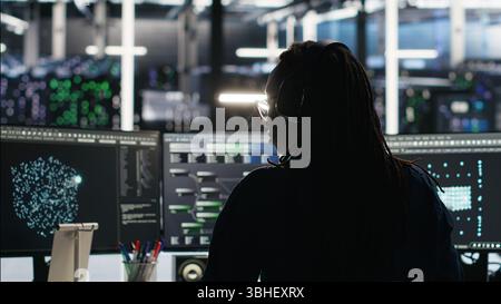 Server room programmer interpreting AI generated data analytics graphs, putting on headphones. Data center IT expert uses artificial intelligence tool showing system metrics, listening music, camera B Stock Photo