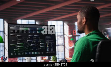 African american software developer does visual coding and creating software, implementing algorithms. IT expert at home working with notes tree and code language, app performance. Camera A. Stock Photo