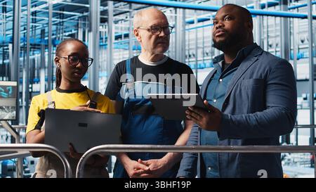 Manager overseeing smart factory, giving instructions to engineers testing automated systems. Industry 4.0 industrial plant supervisor tasking employees with identifying bottlenecks, camera A Stock Photo