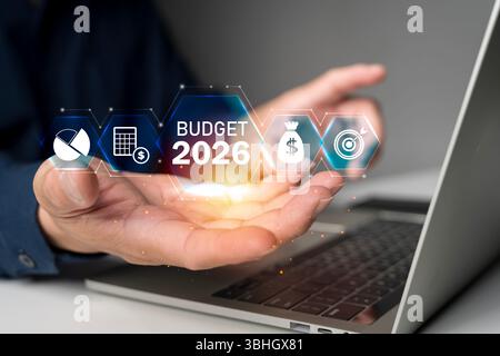 Hand holding virtual budget 2026 interface with finance icons and glowing data on laptop, symbolizing business planning, digital analytics, investment Stock Photo
