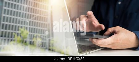Close-up of male hands using smartphone and laptop computer at modern office desk with cityscape reflection, concept of digital communication, remote Stock Photo