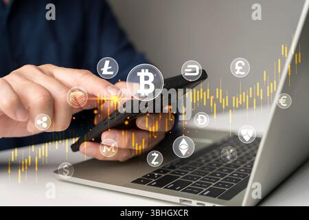 Close-up hand using smartphone with bitcoin, ethereum, and other crypto coin icons, over candlestick trading chart and laptop, representing cryptocurr Stock Photo