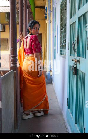 Portrait of a traditional Indian woman wearing a red blouse and yellow saree, accessorized with bangles, earrings, and a nose ring, heritage building Stock Photo