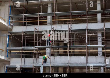 Two male workers assembling scaffolding on a construction site in an urban area during daylight hours Stock Photo