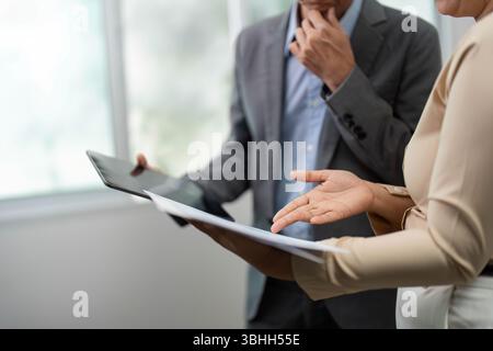 Focused Business Analysis. Colleagues discussing project details with documents and tablet. Stock Photo