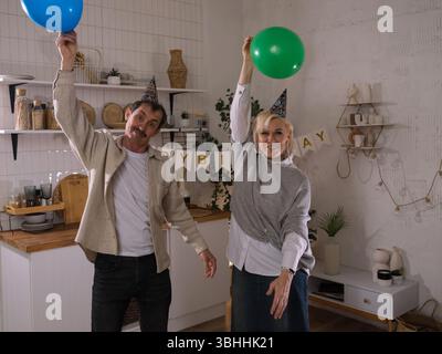 Senior couple wearing party hats and holding balloons celebrating birthday Stock Photo