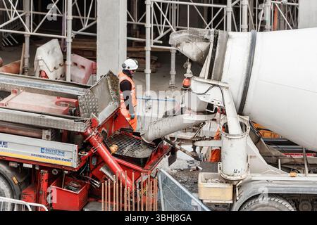 Construction worker in safety gear operating concrete mixers at a busy construction site with scaffolding in the background newcastle upon tyne Stock Photo
