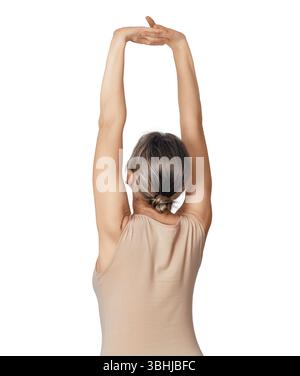 Side view of slim woman stretching arms and back. Woman in beige shirt standing on white background with arms raised. Workout concept Stock Photo