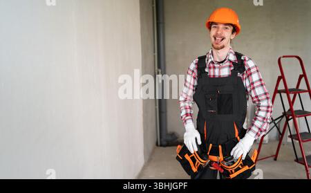 construction site worker wearing safety helmet showing tongue up comic facial expression. Portrait of builder at workplace Stock Photo