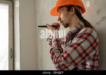 Young builder with smartphone at site for communication or construction making voice note Stock Photo