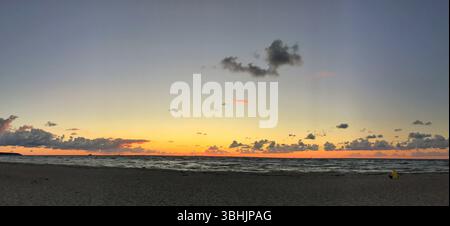 Wide-angle view of a tranquil beach at sunset with warm colors in the horizon and soft waves. Stock Photo